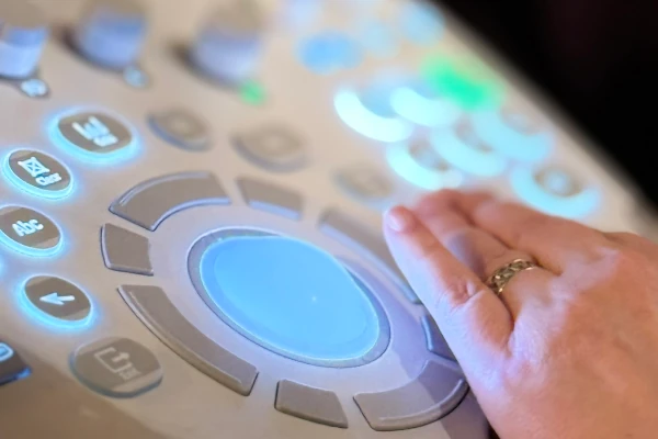 Detalhe de painel eletrônico de equipamento médico com mãos da médica operando os controles.